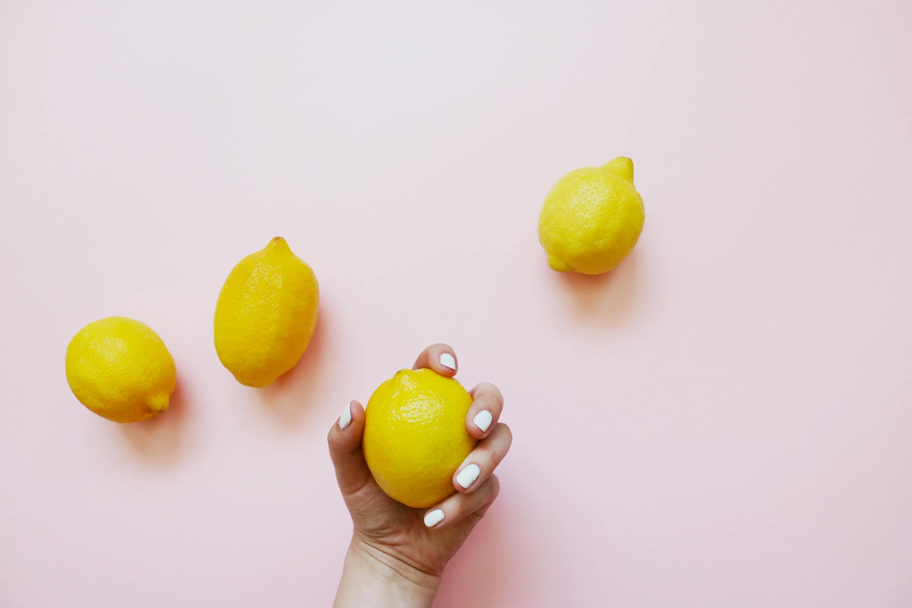 A hand holding a fresh lemon on a soft pink background, symbolizing natural pleasure and vitality.